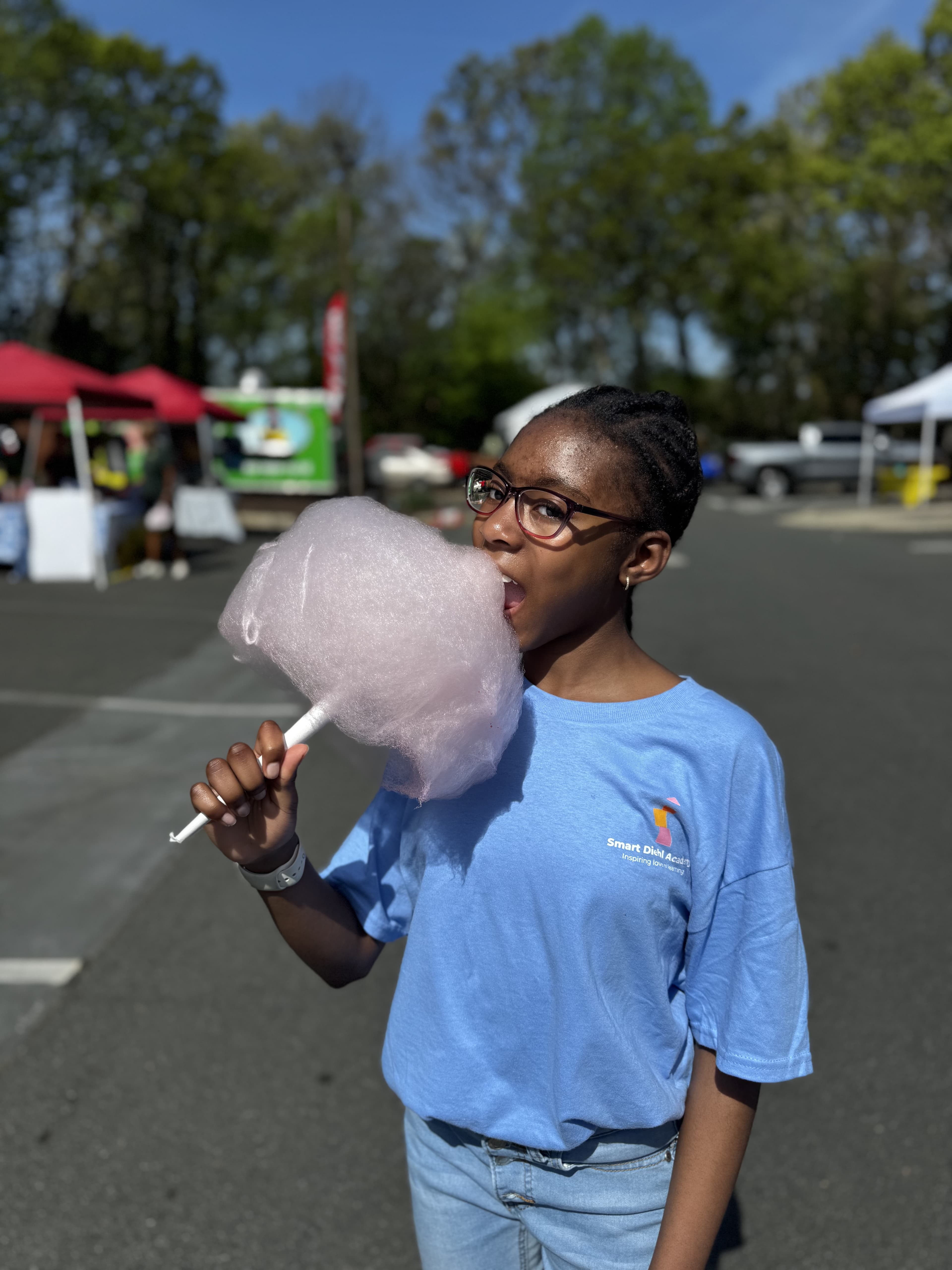 Girl in an SDA t-shirt enjoying cotton candy outdoors at SmartFest