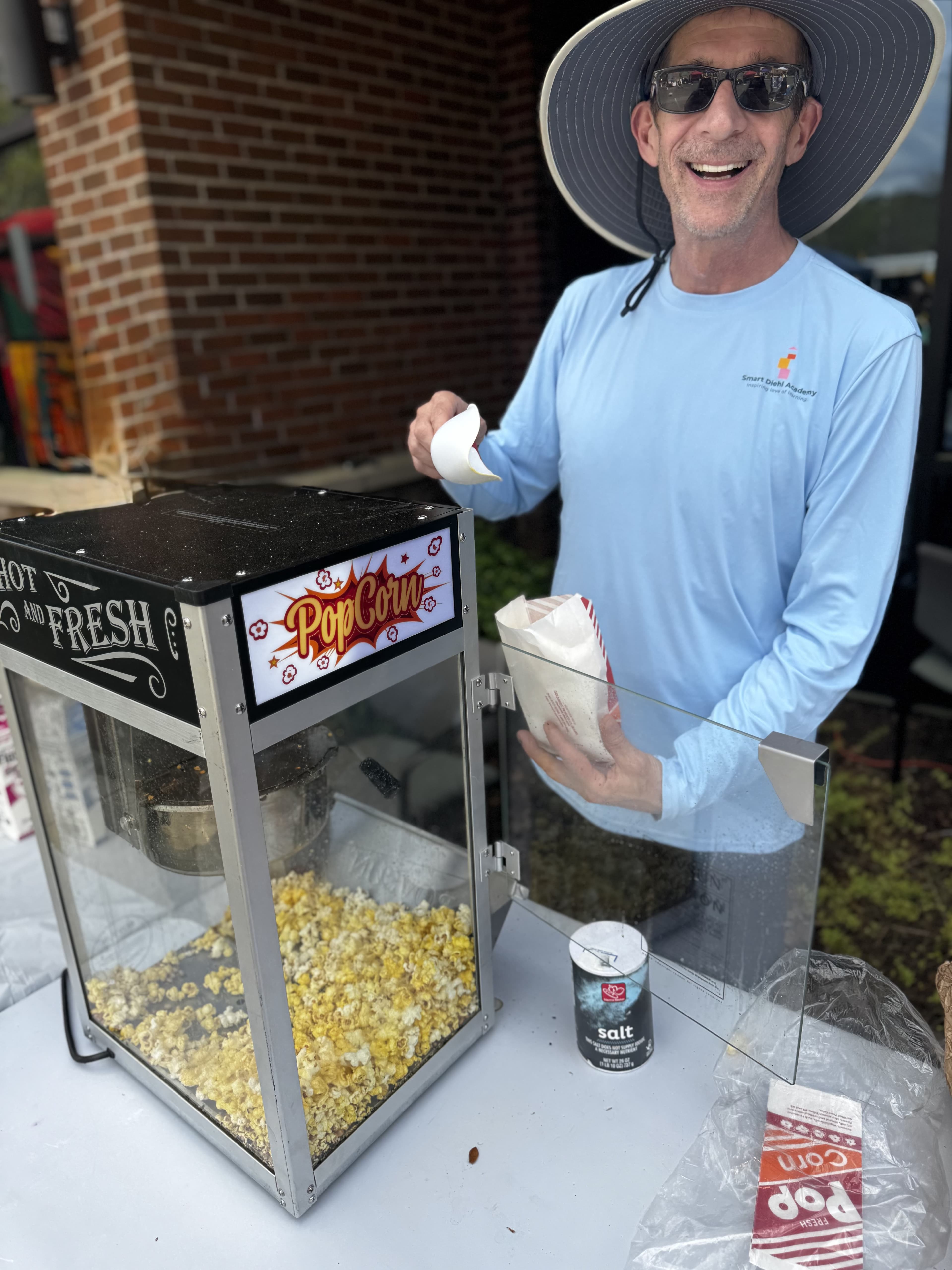 Man in an SDA shirt and hat smiling while serving popcorn at SmartFest