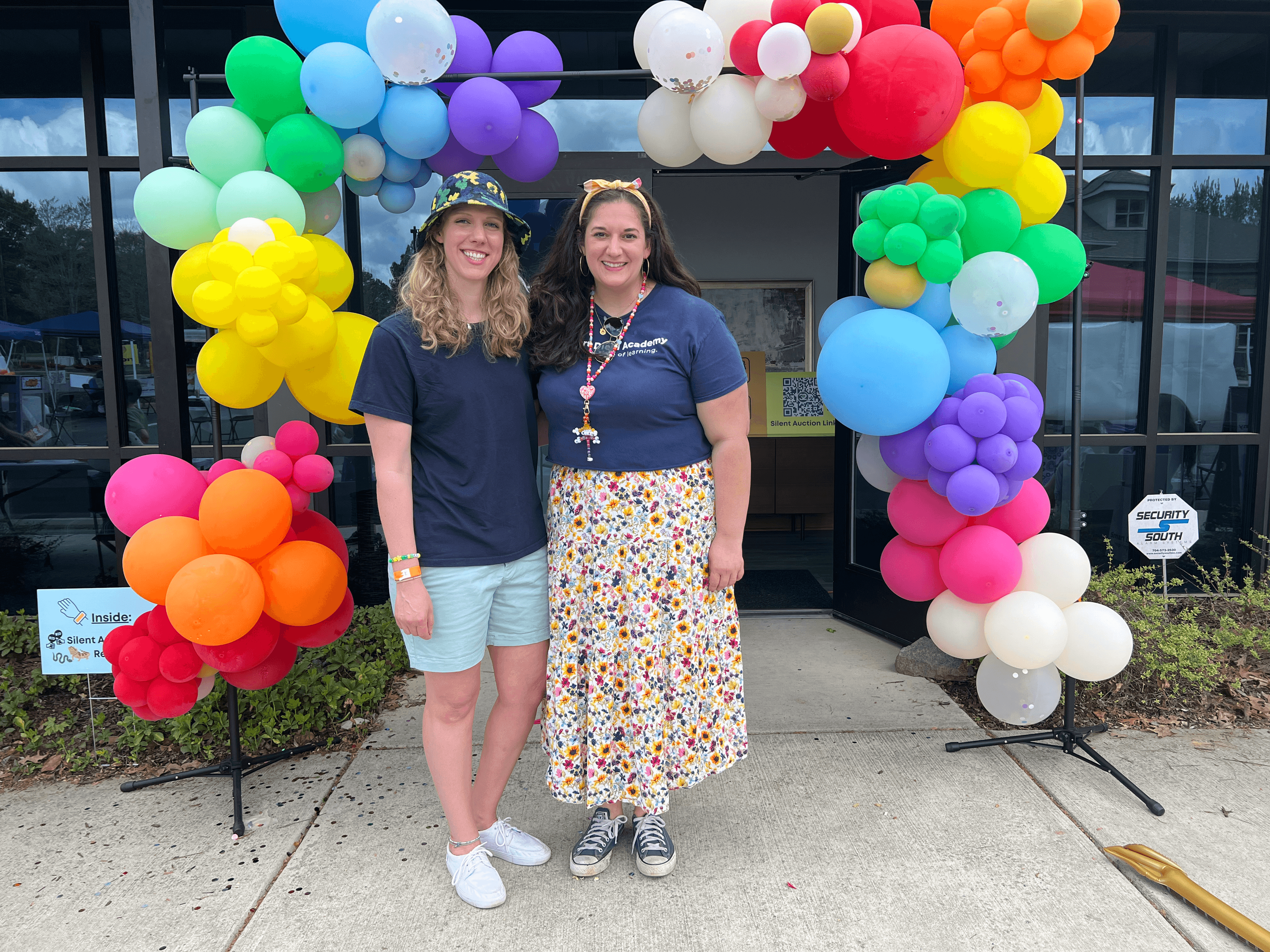 Two SmartFest staff members posing under the colorful rainbow balloon arch entrance